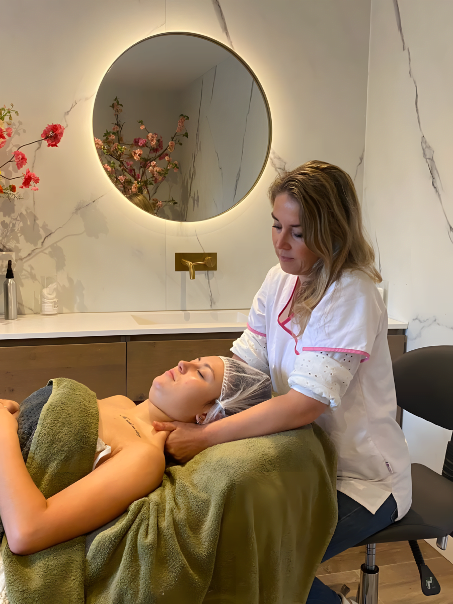 Maaike geeft een nek- en schoudermassage aan een klant die onder een groene handdoek op de behandelstoel ligt