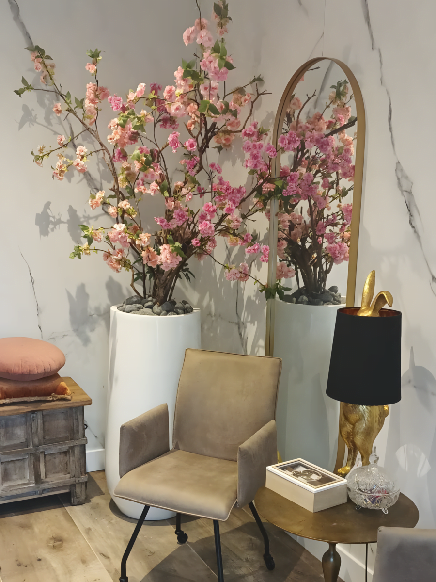 Zithoek in de salon met roze bloesemtakken in witte potten, een hoge spiegel met gouden rand en een fluwelen stoel